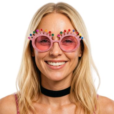 Personne souriante portant des lunettes de soleil fantaisie roses à paillettes avec une monture en forme de couronne ornée de gemmes colorées | jourdefete.com Personne souriante portant des lunettes de soleil fantaisie roses à paillettes avec une monture en forme de couronne ornée de gemmes colorées | jourdefete.com